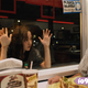 A girl stares through a diner window at a person eating food.